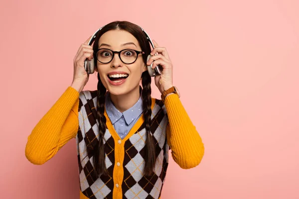 Excited female nerd in eyeglasses listening music with headphones on pink — Stock Photo