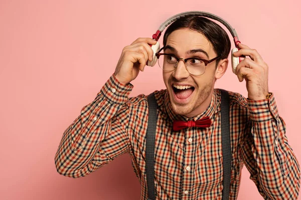 Збуджений чоловічий ботанік в окулярах слухає музику з навушниками на рожевому — стокове фото