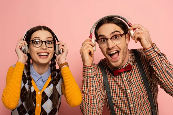 Couple of excited nerds in eyeglasses listening music with headphones on pink — Stock Photo