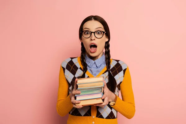 Chocado nerd feminino com boca aberta segurando livros em rosa — Fotografia de Stock