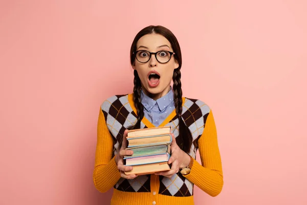 Nerd femelle choqué avec bouche ouverte tenant des livres sur rose — Photo de stock