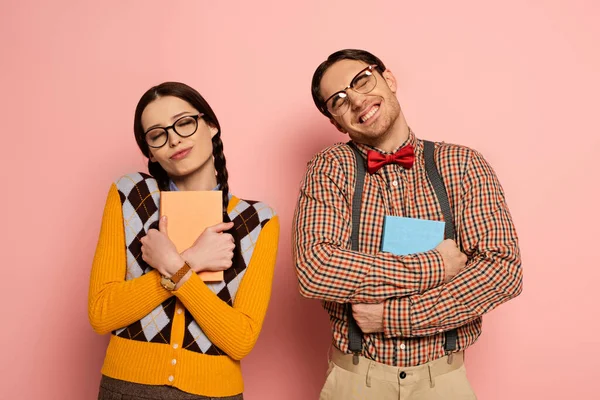 Couple of cheerful nerds in eyeglasses hugging books on pink — Stock Photo