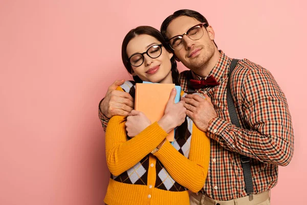 Feliz nerd con los ojos cerrados abrazando novia con libros en rosa - foto de stock