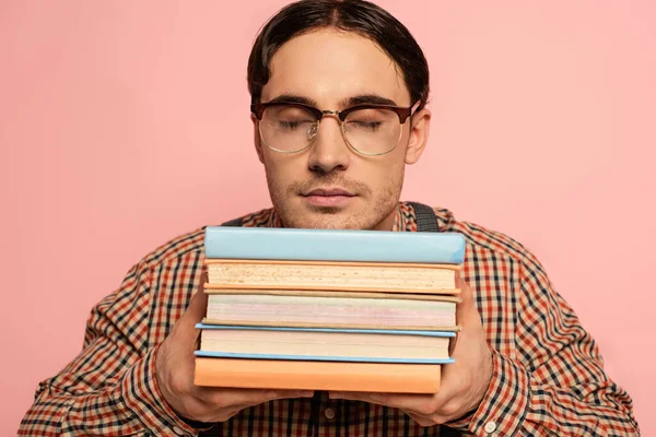 Чоловічий ботанік в окулярах з закритими очима тримає книги, ізольовані на рожевому — стокове фото