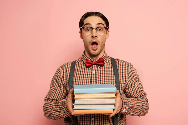 Scioccato nerd maschio con la bocca aperta in occhiali che tengono libri su rosa — Foto stock