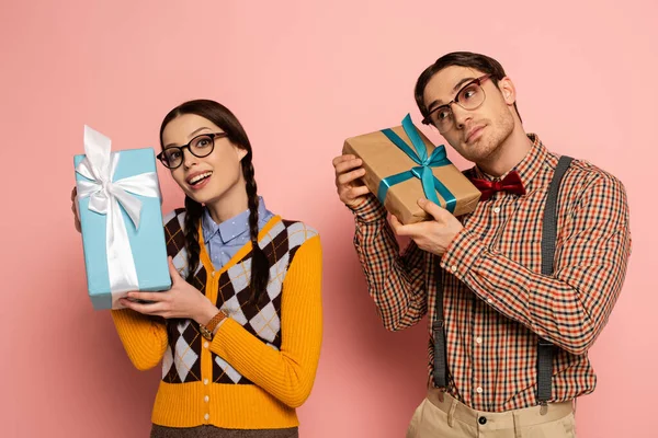 Couple of emotional nerds in eyeglasses holding gifts on pink — Stock Photo