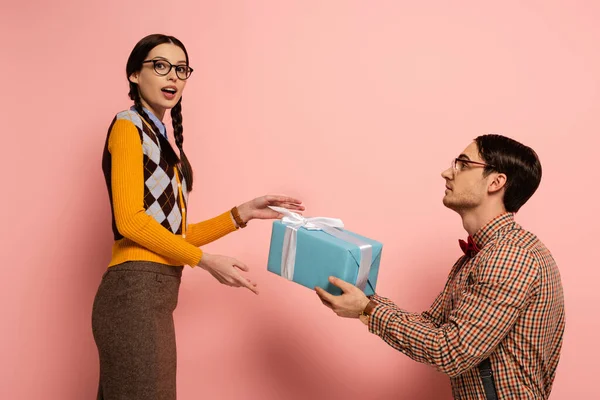 Guapo nerd dando regalo a sorprendido novia en rosa - foto de stock