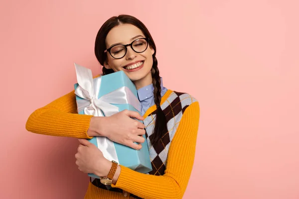 Happy female nerd in eyeglasses holding gift box on pink — Stock Photo