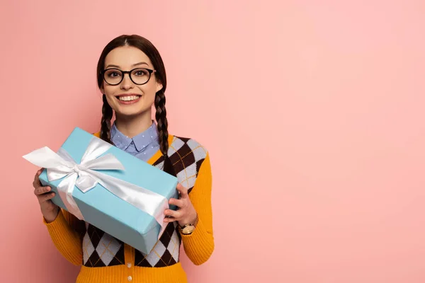 Sonriente nerd femenino en gafas sosteniendo caja de regalo en rosa - foto de stock