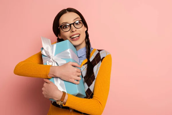 Excited female nerd in glasses holding present on pink — Stock Photo