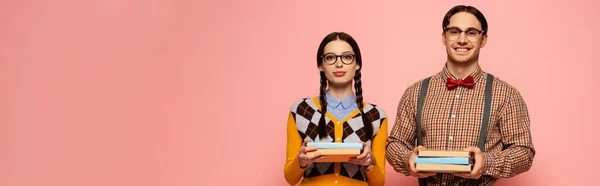 Plan panoramique de couple de geeks heureux dans des lunettes tenant des livres, isolé sur rose — Photo de stock