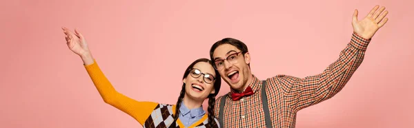 Panoramic shot of couple of happy nerds in eyeglasses gesturing and hugging, Isolated on pink — Stock Photo