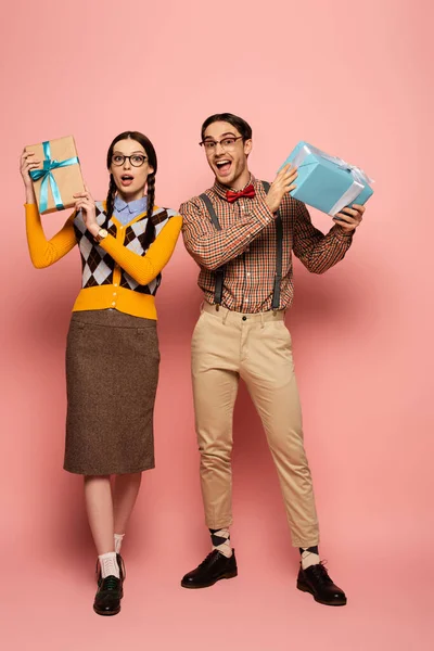 Couple of shocked nerds holding gift boxes on pink — Stock Photo