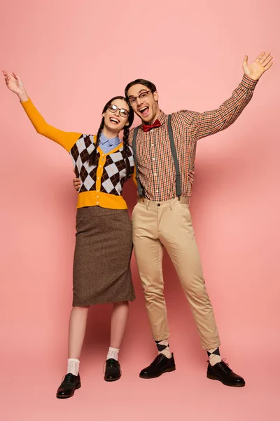 Couple of cheerful nerds in eyeglasses gesturing and hugging on pink — Stock Photo