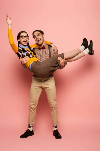 Excited nerd in eyeglasses holding girlfriend on hands on pink — Stock Photo