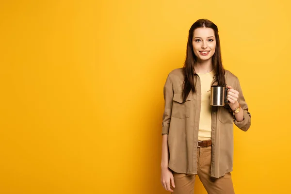 Красива усміхнена жінка мандрівник тримає чашку кави на жовтому — стокове фото