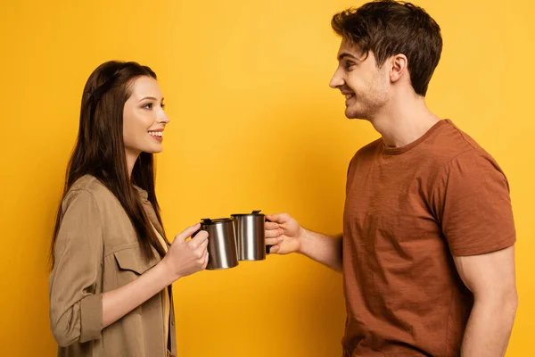 Пара улыбающихся туристов, держащих чашки с кофе на желтом — стоковое фото