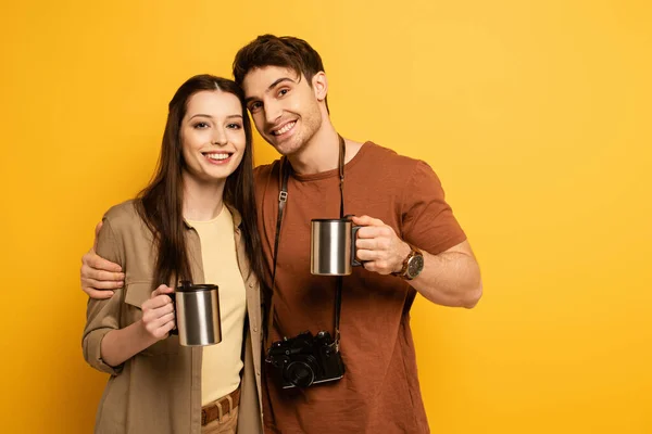 Couple of smiling tourists with photo camera holding cups with coffee on yellow — Stock Photo