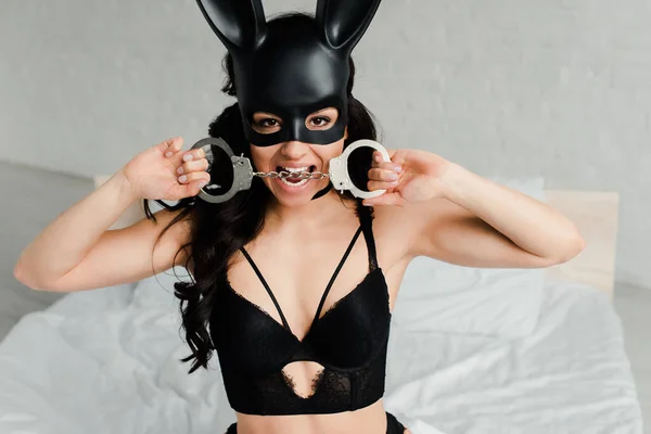 Sexy female submissive in erotic rabbit mask biting handcuffs in bed — Stock Photo