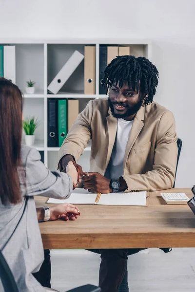Vista recortada del reclutador afroamericano estrechando la mano con el empleado en la entrevista de trabajo en la oficina - foto de stock