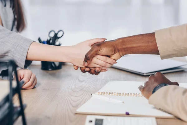 Vista recortada del reclutador afroamericano estrechando la mano con el empleado sobre la mesa en la oficina - foto de stock