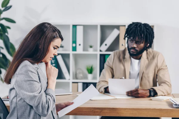 Recruteur afro-américain regardant un employé effrayé avec des papiers à table au bureau — Photo de stock