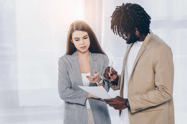 Reclutador y empleado afroamericano con pluma discutiendo documento en la oficina - foto de stock