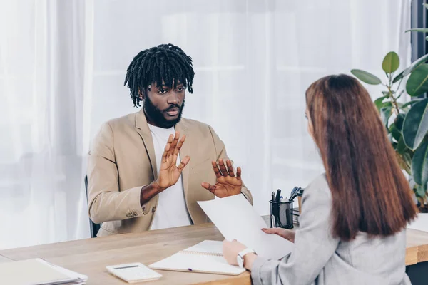 Focus selettivo del reclutatore con carta e dipendente afroamericano che parla al colloquio di lavoro in ufficio — Foto stock