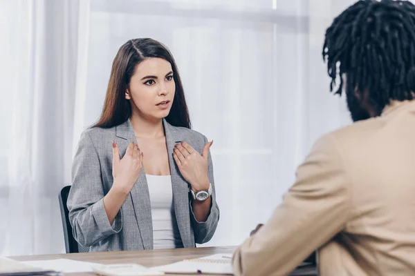 Selective focus of employee pointing oneself and talking to african american recruiter at job interview in office — Stock Photo