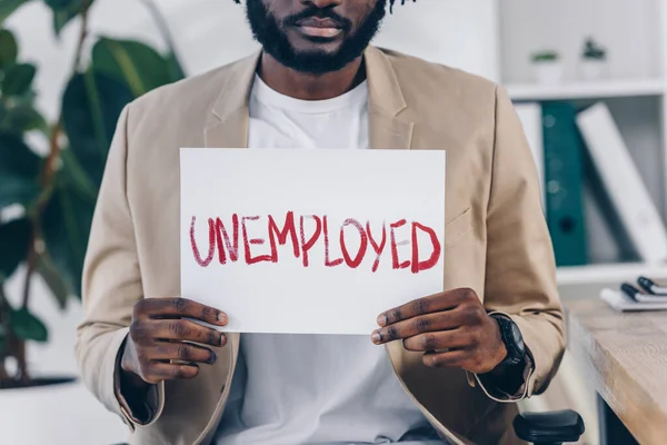 Cropped view of african american employee showing placard with unemployed lettering in office — Stock Photo