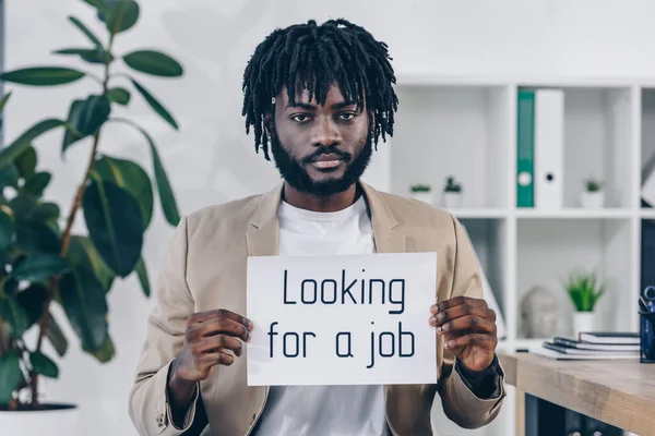 Employé afro-américain montrant la plaque avec la recherche d'un emploi lettrage dans le bureau — Photo de stock