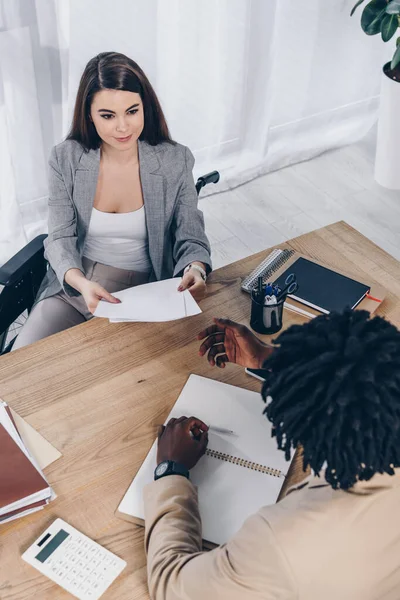 Hochwinkelaufnahme eines behinderten Mitarbeiters, der einem afrikanisch-amerikanischen Personalvermittler bei einem Vorstellungsgespräch im Büro Papiere gibt — Stockfoto