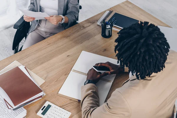 Empleado discapacitado con papeles y reclutador afroamericano con smartphone en entrevista de trabajo - foto de stock