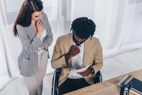 Visão de alto ângulo de funcionário atencioso perto de recrutador de deficientes afro-americano com papéis no escritório — Fotografia de Stock