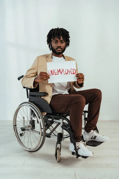 Американский инвалид-американец смотрит в камеру с плакатом с безработными надписью на инвалидном кресле на белом — стоковое фото