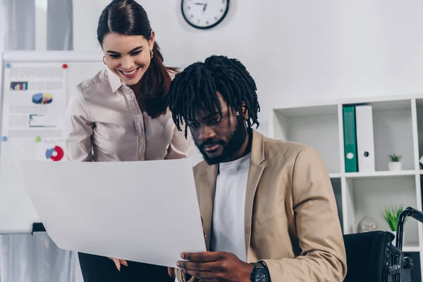 Positive recruiter and african american disabled employee looking at wove paper in office — Stock Photo