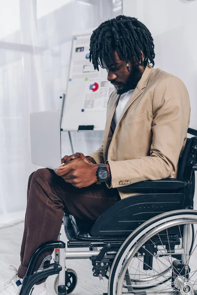 Foco seletivo do funcionário com deficiência afro-americano em cadeira de rodas trabalhando no laptop no escritório — Fotografia de Stock
