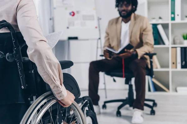 Vista ritagliata del reclutatore disabile su sedia a rotelle e dipendente afroamericano con notebook in ufficio — Foto stock