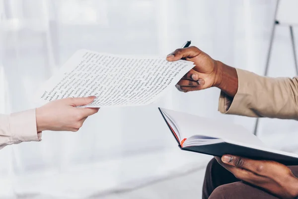 Vista cortada do empregado americano africano com caderno dando papéis para recrutar no escritório — Fotografia de Stock