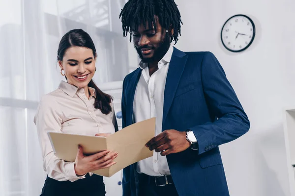 Vista ad angolo basso dei reclutatori multietnici che tengono la cartella aperta e sorridono in ufficio — Foto stock