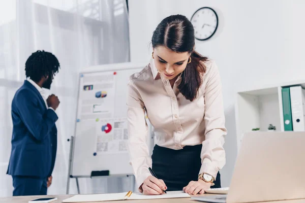 Recruiter writing in notebook and african american employer near flip chart in office — Stock Photo