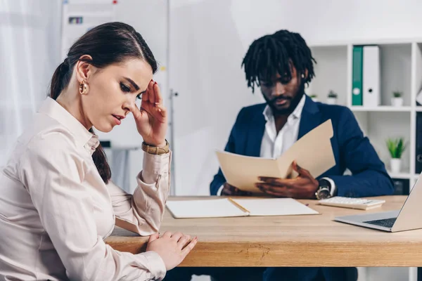 Stressed employee and african american recruiter with folder at table in office — Stock Photo