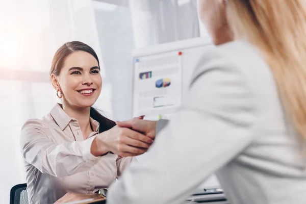 Reclutador sonriendo y estrechando la mano con el empleado en la entrevista de trabajo en la oficina - foto de stock