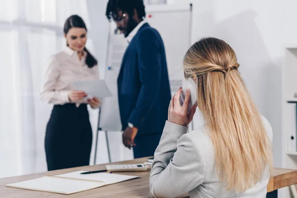 Multicultural recruiters with paper near flip chart and employee talking on smartphone in office — Stock Photo