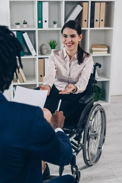 Selective focus of african american recruiter with paper and pen conducting job interview with disabled employee in office — Stock Photo
