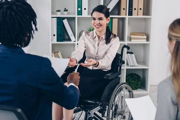 Selective focus of african american recruiter giving paper and pen to disabled employee in office — Stock Photo