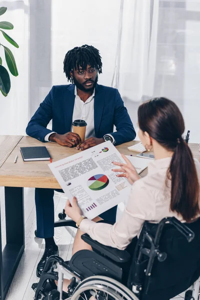 High angle view of african american recruiter and disabled employee with paper on wheelchair talking at table in office — Stock Photo