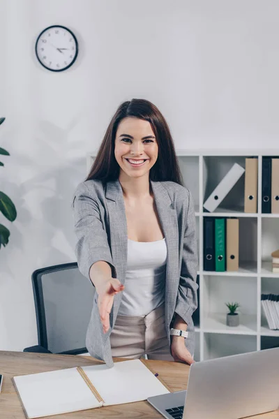 Recruiter with outstretched hand looking at camera and smiling at table in office — Stock Photo