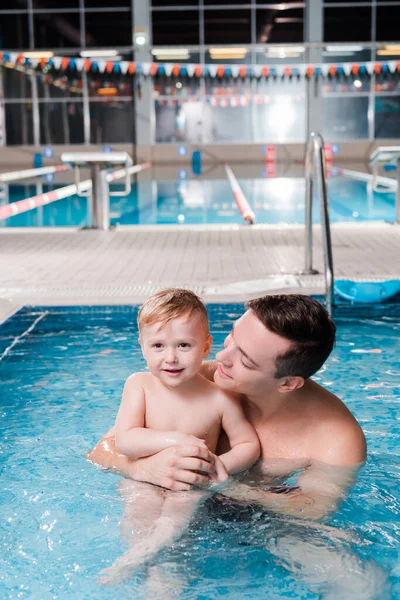 Glücklicher Schwimmtrainer schaut niedlichen Kleinkind-Jungen im Schwimmbad an — Stockfoto