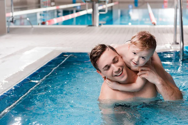 Criança feliz abraçando treinador de natação na piscina — Fotografia de Stock